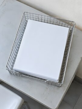 Wire mesh in tray on a tuition room side table holding a neat stack of blank sheets