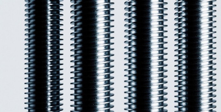 Macro view of vertical steel threaded rods. Parallel metal bolts show repetitive texture, industrial pattern. Shiny silver fasteners with precision screw threads stand in rows. Metallic hardware