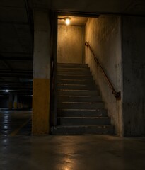 Fototapeta premium Below ground concrete stairwell of a parking garage lit by one caged bulb with painted walls and stained steps