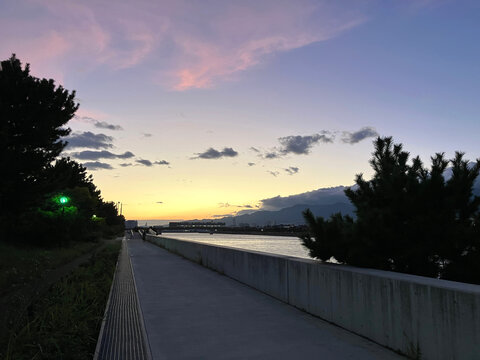 日本の川沿いに続く舗装された遊歩道と夕暮れの空