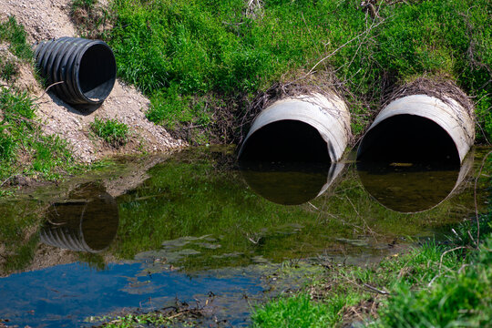 Creek water flows past culvert pipes. Creek drainage supports sustainable wetland balance. Runoff enters creek through drainage system. Flood control protects creek from erosion.