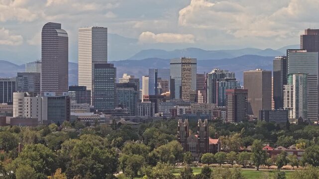 Denver church with skyline with urban buildings, green park, and distant mountain range flying upwards