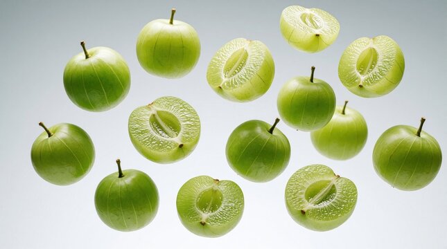 Collection of fresh green Indian gooseberries, some whole and some halved, floating against a clean grey backdrop. This fruit is rich in vitamins and antioxidants, useful for health and wellness.