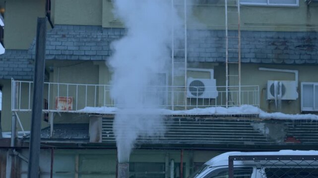 雪が積もる屋根と煙突から立ち上る白い湯気のスローモーション