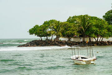 Scenic coastal view of a small canopy boat anchored near palm-covered shoreline in Sri Lanka © Muñe