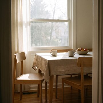 Wooden dining table and chairs set in a sunlit room with a bowl of fresh apples