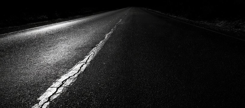 Cracked white line on an empty asphalt road stretching into darkness