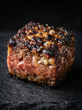 A single cube of seared beef steak on a dark slate background.