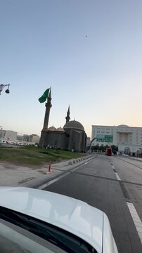 Dashcam view driving past a historic stone mosque and Saudi flag in Madinah.