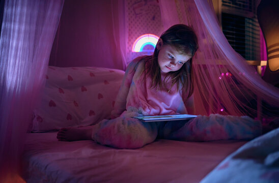 Young girl using tablet in bed at night illuminated by screen light