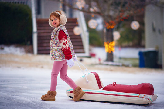 Happy little girl pulling snow tube outdoors on a winter day
