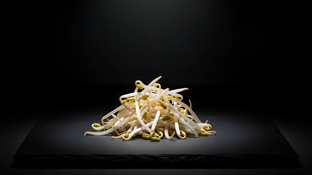 Fresh mung bean sprouts arranged in a small pile on a dark surface with dramatic side lighting highlighting crisp stems yellow tips natural texture healthy food and plant based nutrition