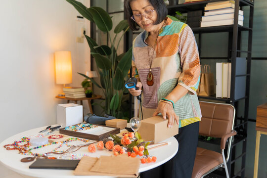 Mature Asian woman using barcode reader scan handcrafted jewelry package