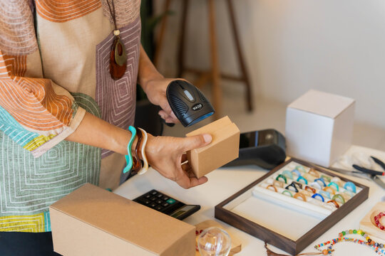 Mature Asian woman using barcode reader scan handcrafted jewelry package
