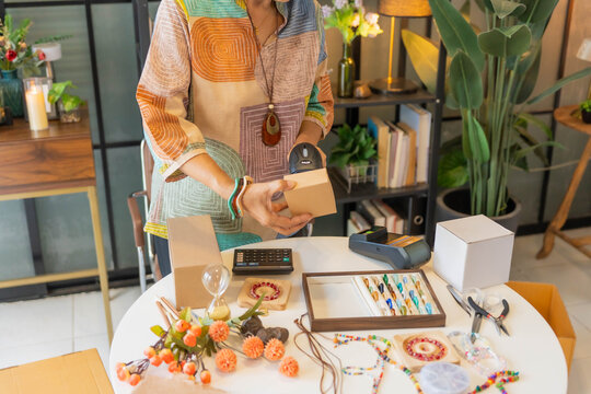 Mature Asian woman using barcode reader scan handcrafted jewelry package