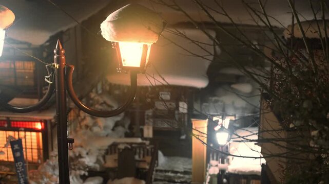 レトロな街灯の温かい明かりが灯る雪降る夜の温泉街のスローモーション