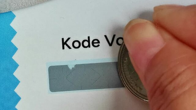 Hand scratching off voucher code on card with coin close up