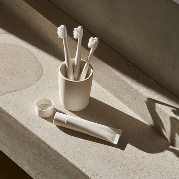 Unbranded toothbrushes in a ceramic cup on a stone bathroom counter