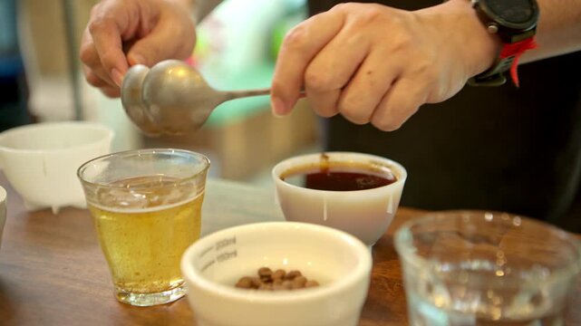 A barista is using a spoon to skim the coffee grounds floating on the surface of the brewed coffee, preparing it for a Q-Grader to taste