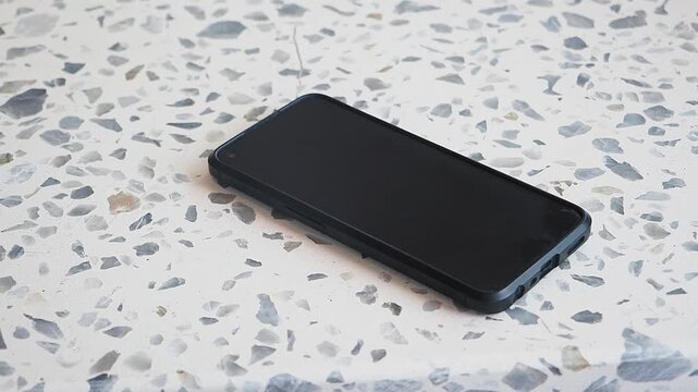 Hand Picking Up a Smartphone from a Terrazzo Surface