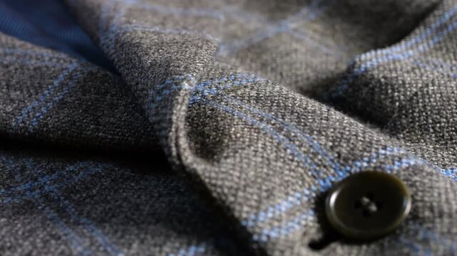 A close-up of a grey tweed woolen jacket lapel highlights fine lining material, elegant buttons, professional tailoring techniques, suiting material texture, and fashion details.