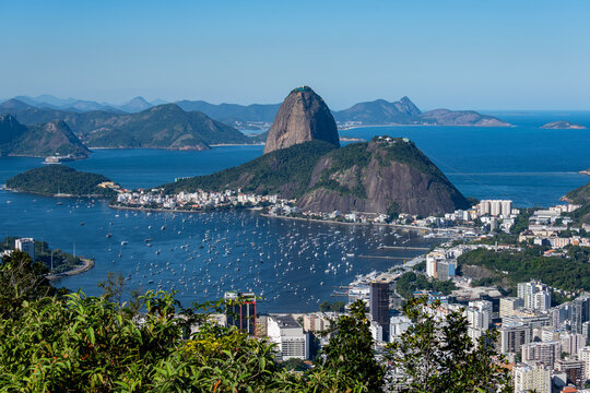 The sweeping view of Sugarloaf Mountain highlights its imposing shape rising above Guanabara Bay, featuring green slopes, blue waters, and the sprawling city. Rio de Janeiro, Brazil.	
