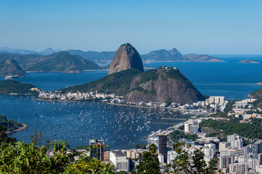 The sweeping view of Sugarloaf Mountain highlights its imposing shape rising above Guanabara Bay, featuring green slopes, blue waters, and the sprawling city. Rio de Janeiro, Brazil.	
