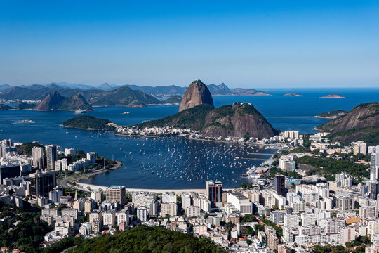 The sweeping view of Sugarloaf Mountain highlights its imposing shape rising above Guanabara Bay, featuring green slopes, blue waters, and the sprawling city. Rio de Janeiro, Brazil.	
