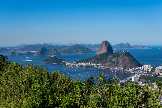 The sweeping view of Sugarloaf Mountain highlights its imposing shape rising above Guanabara Bay, featuring green slopes, blue waters, and the sprawling city. Rio de Janeiro, Brazil.	
