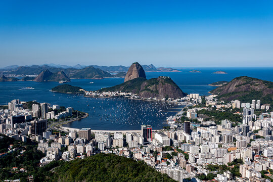 The sweeping view of Sugarloaf Mountain highlights its imposing shape rising above Guanabara Bay, featuring green slopes, blue waters, and the sprawling city. Rio de Janeiro, Brazil.	
