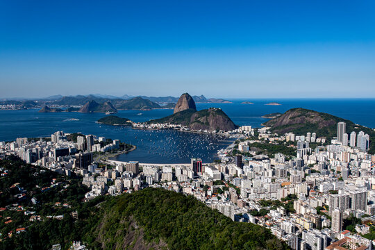 The sweeping view of Sugarloaf Mountain highlights its imposing shape rising above Guanabara Bay, featuring green slopes, blue waters, and the sprawling city. Rio de Janeiro, Brazil.	

