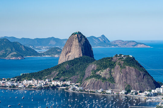The sweeping view of Sugarloaf Mountain highlights its imposing shape rising above Guanabara Bay, featuring green slopes, blue waters, and the sprawling city. Rio de Janeiro, Brazil.	
