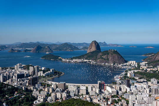 The sweeping view of Sugarloaf Mountain highlights its imposing shape rising above Guanabara Bay, featuring green slopes, blue waters, and the sprawling city. Rio de Janeiro, Brazil.	
