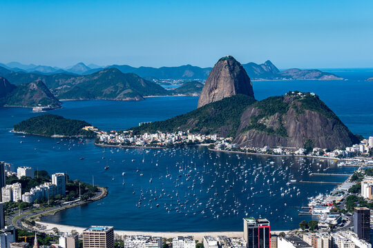 The sweeping view of Sugarloaf Mountain highlights its imposing shape rising above Guanabara Bay, featuring green slopes, blue waters, and the sprawling city. Rio de Janeiro, Brazil.	
