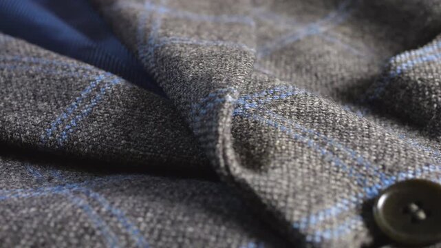 A close-up of a grey tweed woolen jacket lapel highlights fine lining material, elegant buttons, professional tailoring techniques, suiting material texture, and fashion details.