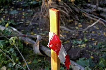 Bright yellow wooden stake marked with red and white caution tape stands in the grass, indicating a designated construction zone or restricted work area © PhotoChur