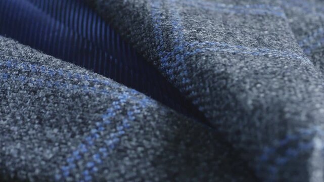 A close-up of a grey-blue tweed woolen jacket lapel showing fine lining material and elegant buttons, highlighting professional tailoring techniques and fabric texture.