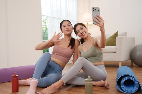 Two Asian women taking a smartphone selfie after a home workout, representing fitness, yoga, friendship, healthy lifestyle and wellness.