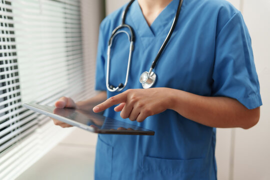 Healthcare professional in blue scrub using digital tablet in a clinic, representing medical technology, exam patient diagnosis, health records.