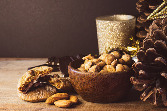 Christmas Eve holiday sweets and dried fruits on a wooden table, featuring almonds, figs, chocolate, and pine cones, celebrating festive traditions
