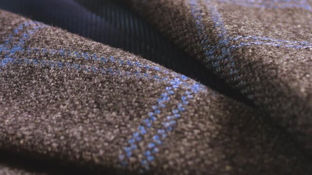 A close-up of a brown tweed woolen jacket lapel showing fine lining material and elegant buttons, highlighting professional tailoring techniques and fabric texture.