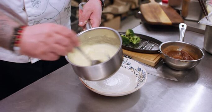 Professional culinary. Polenta recipe. Chef hand stirring hot smooth white porridge in metal saucepan on metal restaurant kitchen table.