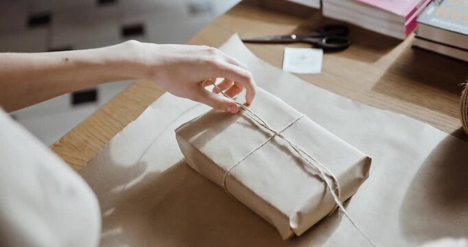 Close-up of Hands Tying a Knot on a Rustic Gift Wrapped in Kraft Paper with Jute Twine on a Wooden Table