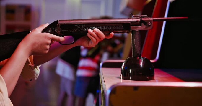 Close-up of a player's hands aiming a vintage light gun controller at an arcade machine in a retro gaming center with atmospheric red neon lighting