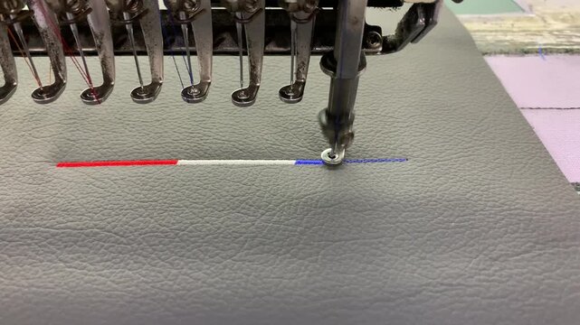Industrial embroidery machine stitching above on textured synthetic leather material.