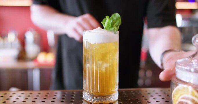 Decorating cocktail. Alcoholic beverage. Man barkeeper hand adding fresh mint green leaves in aroma orange juice whipped cream top.