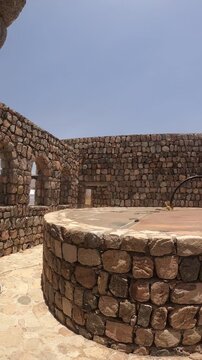 Panning view of ancient stone well ruins and a walled courtyard with archways.