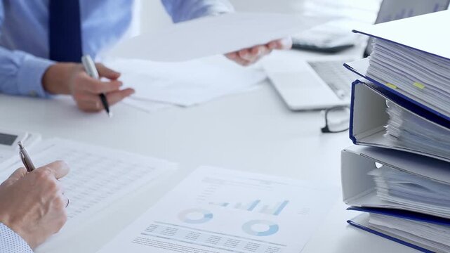 Corporate professionals reviewing financial documents, working collaboratively at white desk with blue folder stack, highlighting teamwork and business productivity. Audit and taxes in business