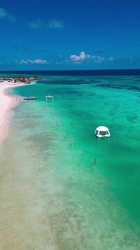 Aerial beach view woman bikini sunbathing relaxed model lies on golden sand under bright sun, turquoise ocean waves lap shoreline, drone captures top down panorama, warm summer,Maldives,vertical video