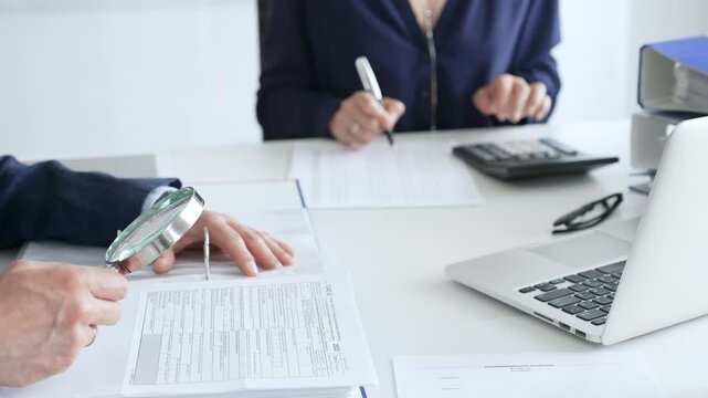 Two professional chartered accountants reviewing financial reports and analyzing data using a calculator and a magnifying glass, ensuring accuracy and compliance. Audit and taxes in business